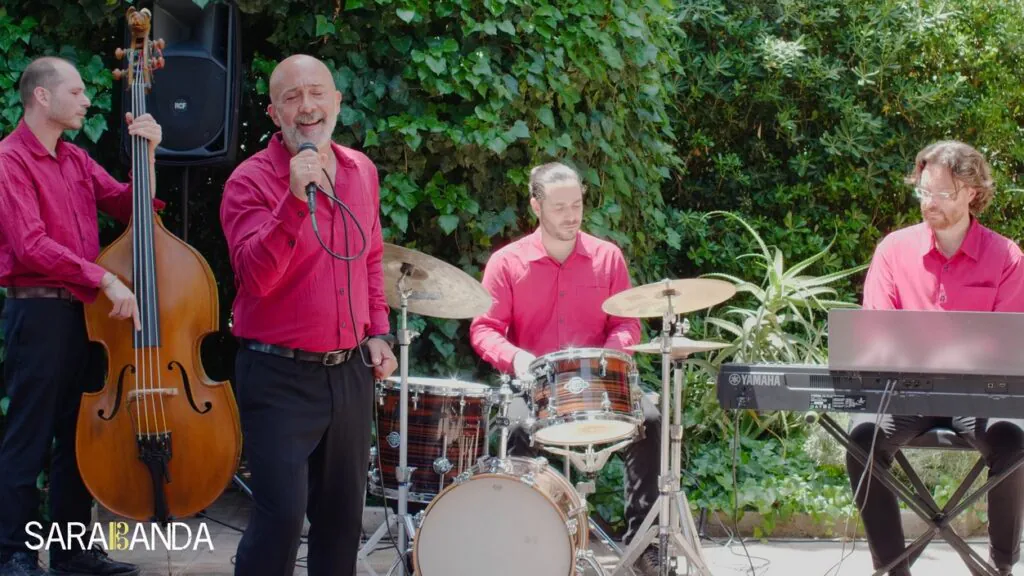 Sarabanda 4tet sul set del video di "L-O-V-E", estate 2025. In camicia rossa bordeaux su sfondo verde (un gazebo di edera e altre piante)